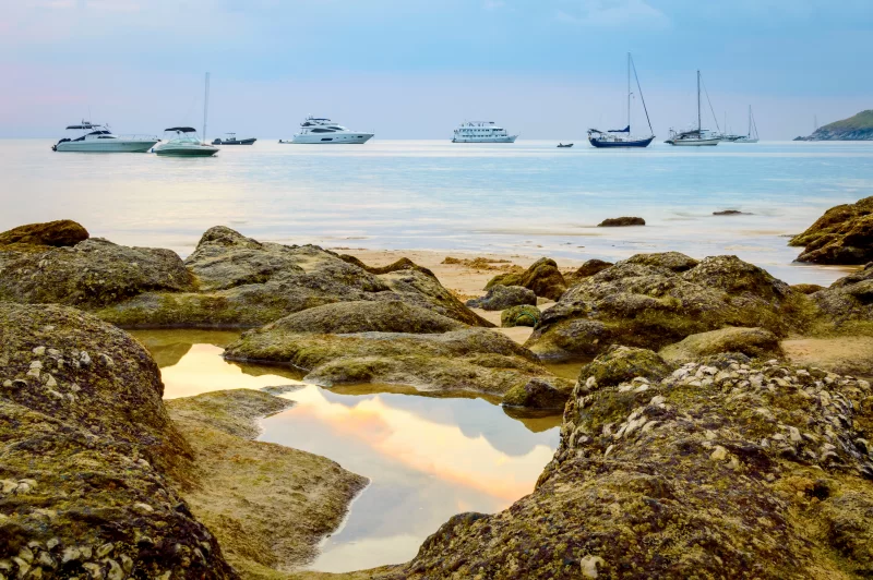 Песчаный пляж с кораллами и яхтами на закате