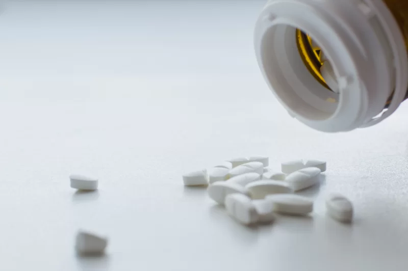 Белые таблетки, высыпающиеся из бутылочки на белую поверхность